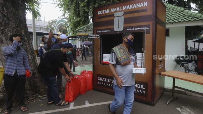 Warga mengambil makanan gratis di Kotak Amal Makanan Gratis di pelataran Masjid Cut Meutia, Jakarta, Jumat (11//12/2020). [Suara.com/Angga Budhiyanto]