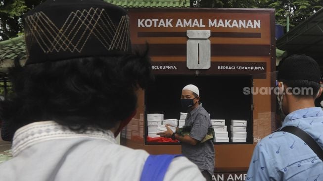 Warga mengambil makanan gratis di Kotak Amal Makanan Gratis di pelataran Masjid Cut Meutia, Jakarta, Jumat (11//12/2020). [Suara.com/Angga Budhiyanto]