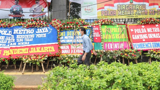 Warga melintas di depan Karangan bunga yang membanjiri halaman depan Polda Metro Jaya, Jakarta Selatan, (12/12). [Suara.com/Alfian Winanto]