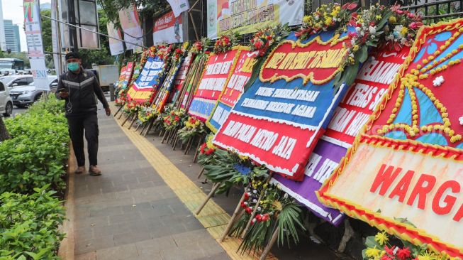 Warga melintas didepan Karangan bunga yang membanjiri halaman depan Polda Metro Jaya, Jakarta Selatan, (12/12). [Suara.com/Alfian Winanto]