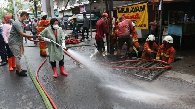 Wali Kota Surabaya Tri Rismaharini (tengah) membersihkan jalan saat kerja bakti pembersihan saluran air di Mulyosari, Surabaya, Jawa Timur, Sabtu (12/12/2020).  ANTARA FOTO/Didik Suhartono
