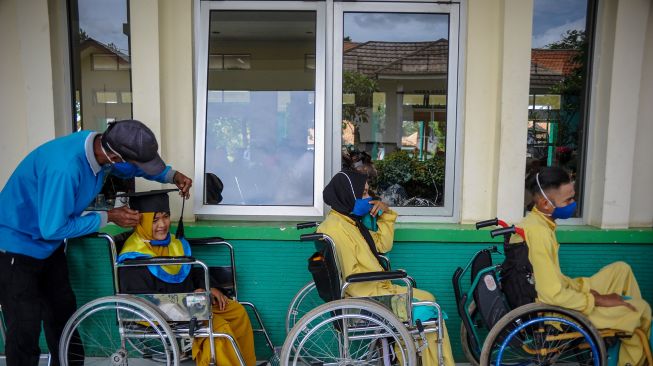 Seorang pendamping membetulkan posisi topi toga seorang siswa disabilitas saat mengikuti wisuda di Panti Sosial Rehabilitasi Penyandang Disabilitas Dinas Sosial Provinsi Jawa Barat, Cimahi, Jawa Barat, Selasa (15/12/2020). [ANTARA FOTO/Raisan Al Farisi]
