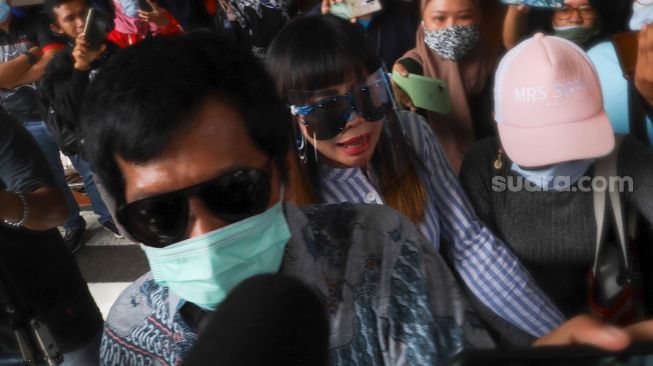 Komedia Kiwil bersama dengan istri mudanya, Eva Bellissima mencoba menghindari awak media saat tiba di Terminal 2 Bandara Soekarno Hatta, Tangerang, Banten, Rabu (16/12). [Suara.com/Alfian Winanto]