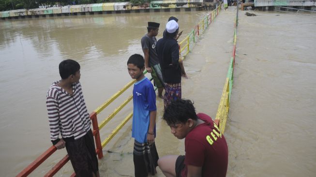 Warga berada di atas jembatan kayu yang permukaannya rata dengan air banjir di Desa Laden Pamekasan, Jawa Timur, Sabtu (19/12/2020). [ANTARA FOTO/Saiful Bahri]