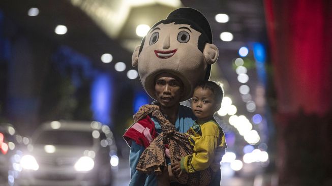 Wahyu (30) menggendong anaknya sambil mengamen sebagai badut di Jalan Pangeran Antasari, Jakarta Selatan, Sabtu (19/12/2020).  [ANTARA FOTO/Sigid Kurniawan]