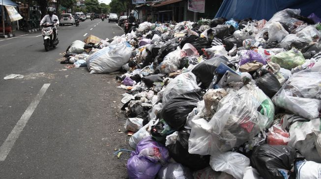 Pengendara melaju di samping tumpukan sampah yang menutupi sebagian sisi jalan raya di tempat pembuangan sementara Lempuyangan, Yogyakarta, Senin (21/12/2020). [ANTARA FOTO/Hendra Nurdiyansyah]
