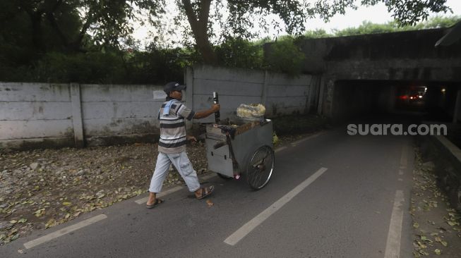 Seorang pedagang berjalan memasuki jalur alternatif di bawah kolong jalan tol Jagorawi di kawasan Terminal Kampung Rambutan, Jakarta, Rabu (23/12/2020). [Suara.com/Angga Budhiyanto]