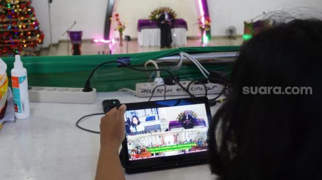 Salah satu operator Gereja HKBP Ciputat mengawasi layar monitor yang digunakan untuk menghubungkan jemaat yang menjalani Misa Natal di gereja maupun secara virtual, Kamis (24/12/2020). [Suara.com/Hairul Alwan]