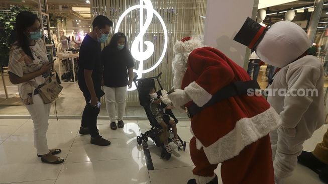 Petugas mengenakan kostum Santa Claus saat menghibur pengunjung di Senayan City Mall, Jakarta, Jumat (25/12/2020). [Suara.com/Angga Budhiyanto]