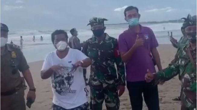 Hotman Paris bersama petugas razia masker di sebuah pantai di Bali. [Instagram]