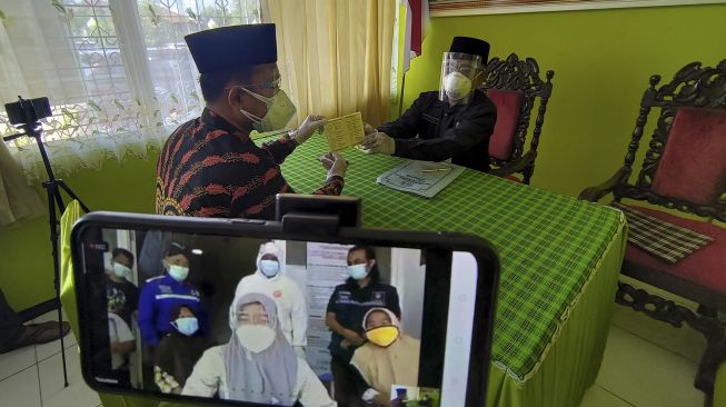 Penghulu yang bertindak sekaligus sebagai wali nikah mempelai perempuan, menyerahkan buku nikah kepada mempelai laki-laki di Kantor Urusan Agama Kecamatan Pakel, Tulungagung, Jawa Timur, Sabtu (26/12/2020). [ANTARA FOTO/Destyan Sujarwoko]