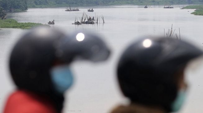 Pengendara sepeda motor melintas di atas jembatan Semampir dengan latar belakang aktivitas penambangan pasir sungai Brantas di Kota Kediri, Jawa Timur, Senin (28/12/2020). [ANTARA FOTO/Prasetia Fauzani]
