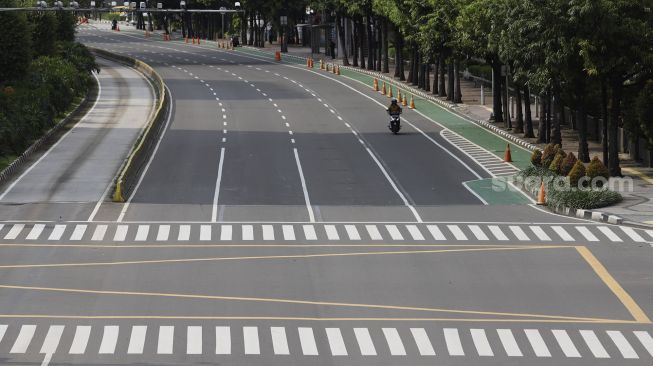 Pengendara sepeda motor melintas saat masa pembatasan sosial berskala besar (PSBB) di Jalan M.H. Thamrin, Jakarta, Rabu (1/4/2020). [Suara.com/Angga Budhiyanto]