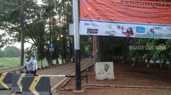 Warga melewati penutup jalan usai berolahraga di kawasan Banjir Kanal Timur (BKT), Jakarta Timur, Jumat (1/1/2020). [Suara.com/Alfian Winanto]