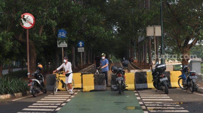 Warga mendorong sepedanya melewati penutup jalan untuk berolahraga di kawasan Banjir Kanal Timur (BKT), Jakarta Timur, Jumat (1/1/2020). [Suara.com/Alfian Winanto]