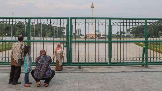 Warga berswafoto bersama keluarganya di belakang Monumen Nasional atau Monas di Jakarta Pusat, Sabtu (2/1/2021). [Suara.com/Alfian Winanto]