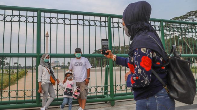 Warga berswafoto bersama keluarganya di belakang Monumen Nasional atau Monas di Jakarta Pusat, Sabtu (2/1/2021). [Suara.com/Alfian Winanto]