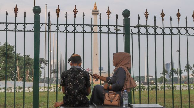 Warga berswafoto di belakang Monumen Nasional atau Monas di Jakarta Pusat, Sabtu (2/1/2021). [Suara.com/Alfian Winanto]