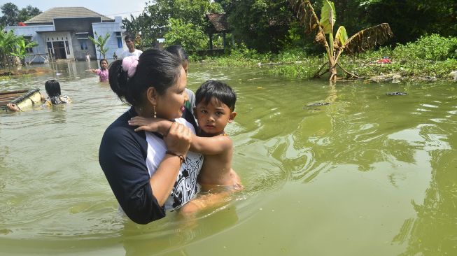 Warga melintasi jalan yang tergenang banjir akibat jebolnya tanggul Sungai Gelis di Desa Setrokalangan, Kudus, Jawa Tengah, Minggu (3/1/2021). [ANTARA FOTO/Yusuf Nugroho]