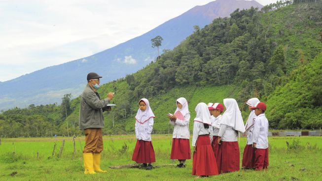 Seorang guru memberikan materi luar kelas kepada beberapa muridnya di SDN 226/III Renah Kasah, Kerinci, Jambi, Senin (4/1/2021). [ANTARA FOTO/Wahdi Septiawan]