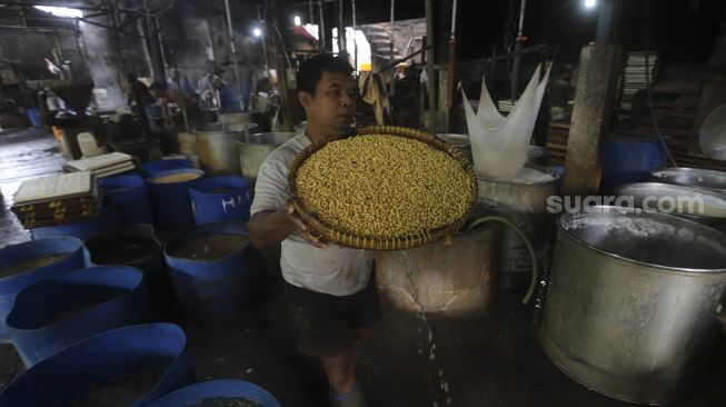 Pekerja mengangkat kacang kedelai saat produksi tahu di salah satu pabrik tahu di kawasan Duren Tiga, Jakarta, Selasa (5/1/2021). [Suara.com/Angga Budhiyanto]