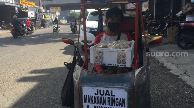 Slamet Nugroho berjualan di atas kursi roda manual yang sudah dimodifikasi di Jalan Raya Tegal-Perwokerto, Kecamatan Adiwerna, Kabupaten Tegal, Rabu (6/1/2021). (Suara.com/F Firdaus)