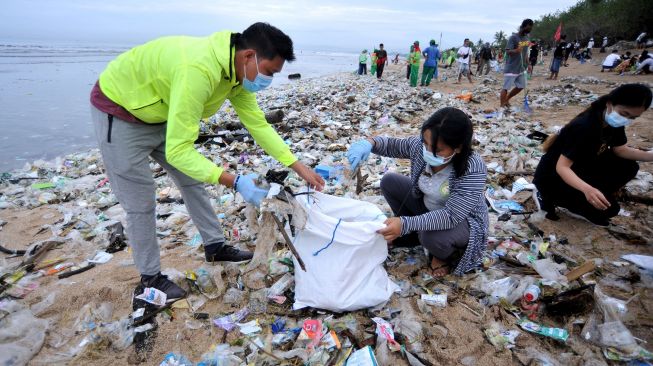 Relawan membersihkan sampah yang berserakan saat mengikuti aksi bersih sampah di Pantai Kuta, Badung, Bali, Rabu (6/1/2021). ANTARA FOTO/Fikri Yusuf