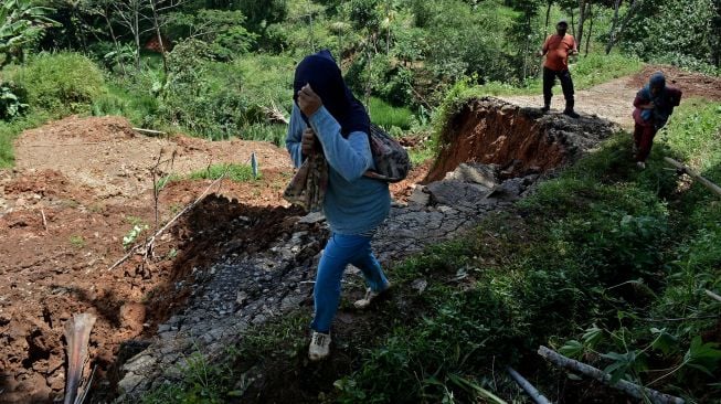 Warga melintas di jalan yang terdampak longsor, di Singajaya, Kabupaten Garut, Jawa Barat, Sabtu (9/1/2021). [ANTARA FOTO/Candra Yanuarsyah]
