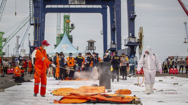 Petugas menyemprotkan cairan disinfektan ke kantong jenazah korban jatuhnya pesawat Sriwijaya Air SJ182 rute Jakarta - Pontianak di Dermaga JICT, Tanjung Priok, Jakarta Utara, Minggu (10/1/2021).  [ANTARA FOTO/Dhemas Reviyanto]