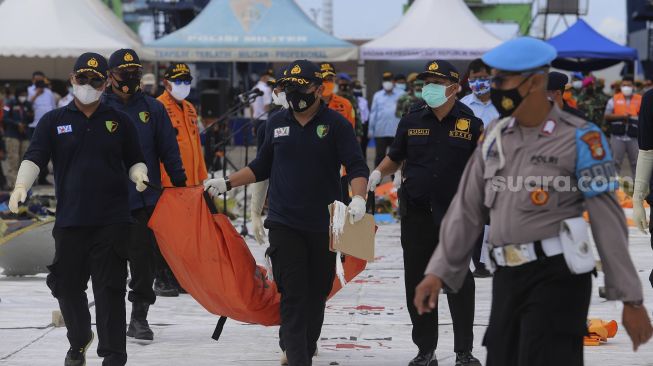 Petugas membawa kantong berisi serpihan dan perlengkapan korban pesawat Sriwijaya Air SJ 182 rute Jakarta - Pontianak yang hilang kontak di perairan Kepulauan Seribu, di Dermaga JICT, Tanjung Priok, Jakarta, Selasa (12/1/2021). [Suara.com/Angga Budhiyanto]