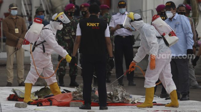 Petugas menyemprotkan cairan disinfektan ke serpihan dan perlengkapan korban pesawat Sriwijaya Air SJ 182 rute Jakarta - Pontianak yang hilang kontak di perairan Kepulauan Seribu, di Dermaga JICT, Tanjung Priok, Jakarta, Selasa (12/1/2021). [Suara.com/Angga Budhiyanto]