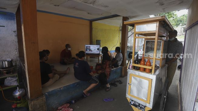 Warga menonton televisi yang menayangkan langsung penyuntikan vaksin CoronaVac perdana di Jakarta, Rabu (13/1/2021). [Suara.com/Angga Budhiyanto]