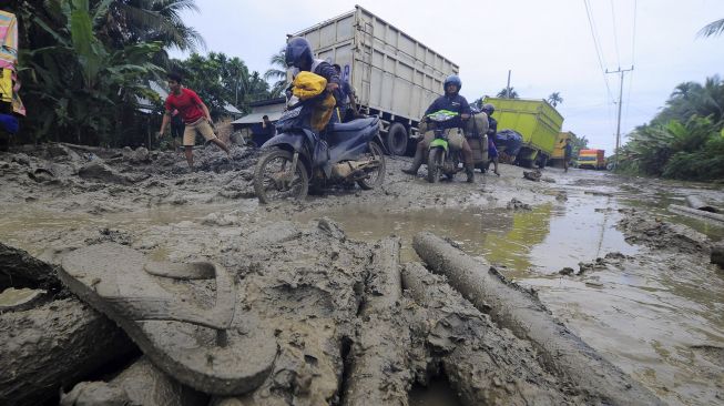 Pengendara mendorong sepeda motornya saat melintasi Jalan Lintas Jambi-Nipah Panjang yang rusak di Siau Dalam, Tanjungjabung Timur, Jambi, Rabu (14/1/2021). [ANTARA FOTO/Wahdi Septiawan]