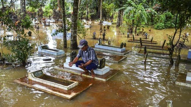 Seorang warga berziarah ke makam keluarganya yang terendam banjir akibat luapan Sungai Citanduy di Tempat Pemakaman Umum (TPU) Desa Kertaraharja, Kecamatan Panumbangan, Kabupaten Ciamis, Jawa Barat, Kamis (14/1/2021). [ANTARA FOTO/Adeng Bustomi]