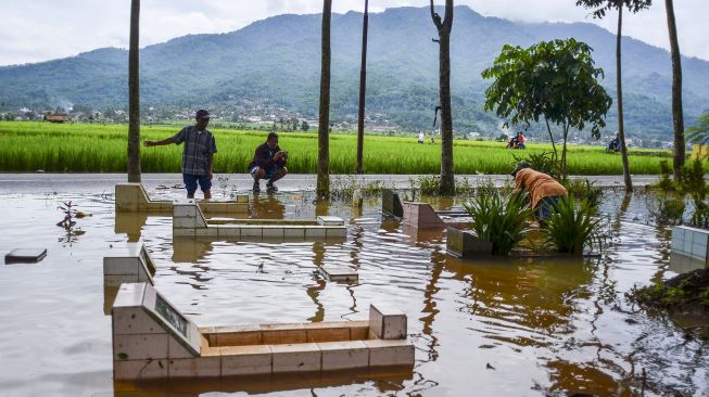 Seorang warga berziarah sambil membersihkan makam keluarganya yang terendam banjir akibat luapan Sungai Citanduy di Tempat Pemakaman Umum (TPU) Desa Kertaraharja, Kecamatan Panumbangan, Kabupaten Ciamis, Jawa Barat, Kamis (14/1/2021). [ANTARA FOTO/Adeng Bustomi]