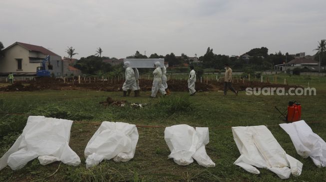 Petugas mengusung peti berisi jenazah yang meninggal dunia karena COVID-19 untuk dimakamkan di TPU Srengseng Sawah, Jakarta, Jumat (15/1/2021). [Suara.com/Angga Budhiyanto]