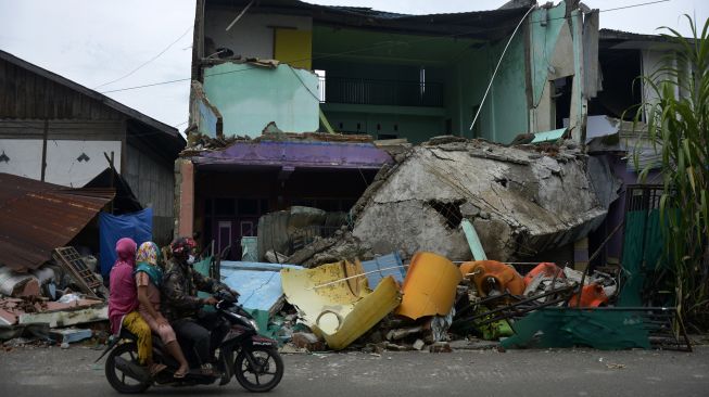 Pengendara melintas di sekitar sebuah rumah yang rusak akibat gempa bumi di Kabupaten Mamuju, Sulawesi Barat, Minggu (17/1/2021).  ANTARA FOTO/Abriawan Abhe