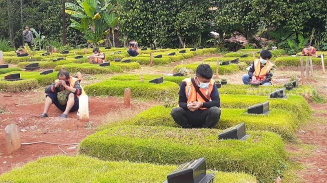 Sejumlah warga yang terjaring razia masker diangkut ke TPU Jombang khusus pemakaman Covid-19 untuk berziarah, Senin (18/1/2021). [Suara.com/Wivy]