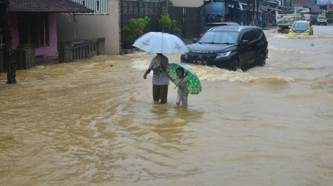 Warga melintasi jalan yang tergenang banjir di Desa Mejobo, Mejobo, Kudus, Jawa Tengah, Selasa (19/1/2021). [ANTARA FOTO]