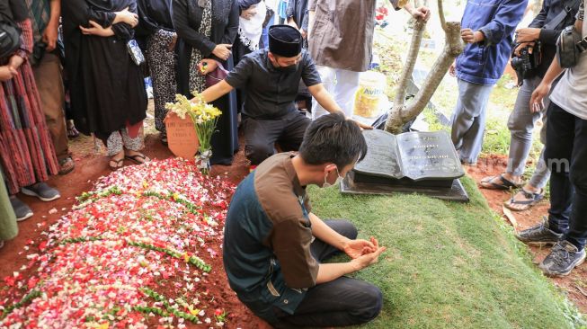 Komedian Denny Cagur berdoa diatas pusara ayah ibunya setelah prosesi pemakaman di TPU Tipar, Depok, Jawa Barat, Selasa (19/1/2021). [Suara.com/Alfian Winanto]