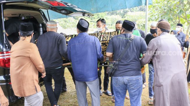 Keranda jenazah ibunda Komedian Denny Cagur dikeluarkan dari ambulan untuk dimakamkan di TPU Tipar, Depok, Jawa Barat, Selasa (19/1/2021). [Suara.com/Alfian Winanto]