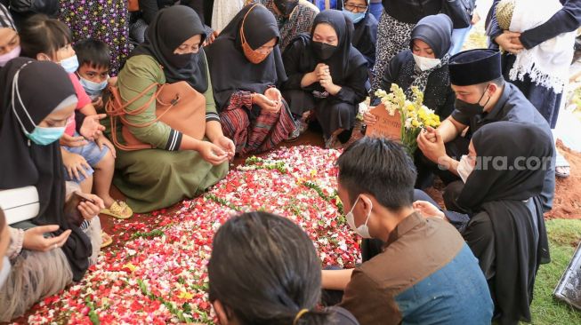 Komedian Denny Cagur bersama dengan keluarga dan kerabat berdoa diatas pusara sang ibu usai dimakamkan di TPU Tipar, Depok, Jawa Barat, Selasa (19/1/2021). [Suara.com/Alfian Winanto]