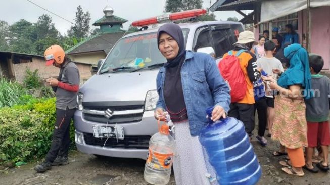 Seorang warga terdampak banjir bandang mencari air bersih ke posko distribusi bantuan pokok di Kampung Rawa Dulang, Puncak Bogor, Rabu (20/1/2021). [Suara.com/Andi Ahmad Sulaendi]