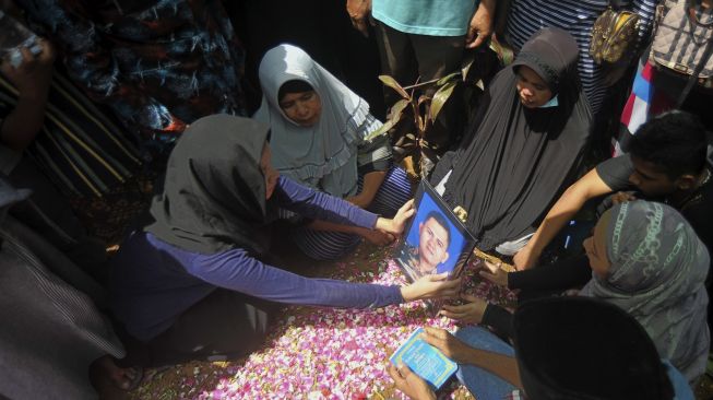 Keluarga memegang foto Angga Fernanda Afriyon di atas pusaranya di Sungai Sapiah, Padang, Sumatera Barat, Sabtu (23/1/2021). [ANTARA/Iggoy el Fitra]