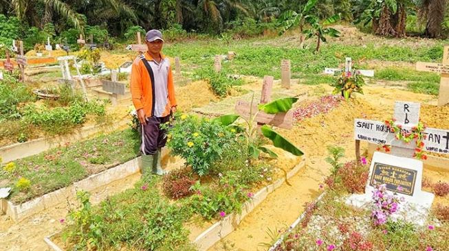 Subhan Zein alias Siken di antara makam korban Covid-19 di TPU Tengku Mahmud Palas, Rumbai, Pekanbaru. [Suara.com/Panji Ahmad Syuhada]