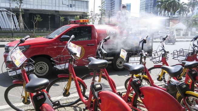 Petugas dari Badan Intelijen Negara (BIN) melakukan penyemprotan cairan disinfektan ke arah sepeda sewa yang berada di Jalan Medan Merdeka Timur, Jakarta, Senin (25/1/2021). ANTARA FOTO/M Risyal Hidayat