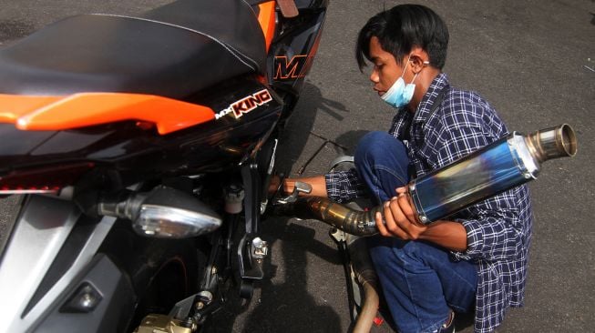 Seorang pengendara melepaskan sendiri knalpot balap dari motornya saat razia di Mapolresta Pontianak, Kalimantan Barat, Senin (25/1/2021). [ANTARA FOTO/Jessica Helena Wuysang]