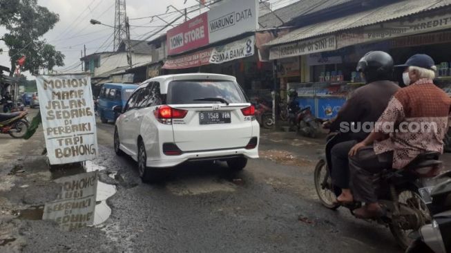 Spanduk bernada sindiran kepada Pemkab Bogor terkait kerusakan Jalan Raya Pabuaran yang merupakan jalan penghubung Kabupaten Bogor-Depok, Senin (25/1/2021). [SuaraBogor.id/Andi Ahmad Sulaendi]