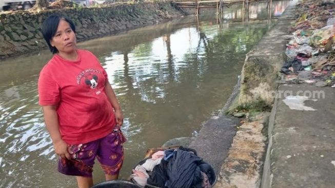 Marliani (40), warga Kampung Melayu, Teluk Naga, Kabupaten Tangerang, tengah mencuci pakaian di kali bercampur sampah, Senin (25/1/2021). [SuaraJakarta.id/Muhammad Jehan Nurhakim]