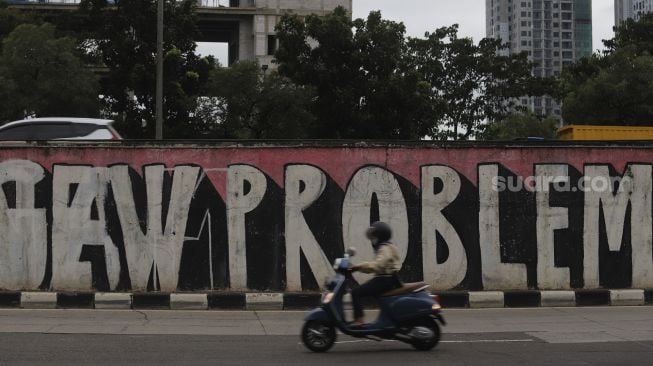 Seorang pengendara sepeda motor melintas di dekat mural bertema tatanan normal baru di Jalan TB Simatupang, Jakarta, Selasa (26/1/2021). [Suara.com/Angga Budhiyanto]